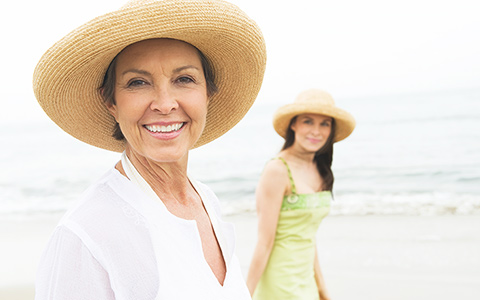 senior mom and her daughter smiling for the camera at the beach